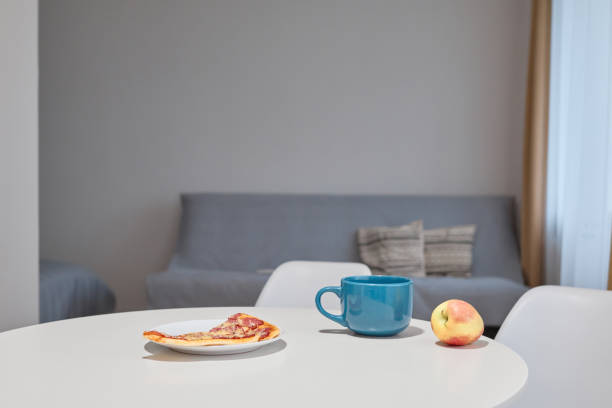 istock Table in kitchen with cup, apple and slice of pizza. Dinner or snack with hot beverage coffee or tea in mug, copy space for advertisement or promotional concept 2164048437