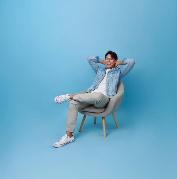 istock asian handsome man relaxing sitting on sofa isolated on blue background. 2164054161