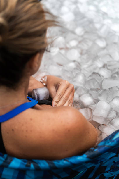 Athlete woman recovering in ice bath after workout session Athlete woman is sitting in a bathtub full of ice, holding a cold pack on her shoulder woman cold water swimming stock pictures, royalty-free photos & images