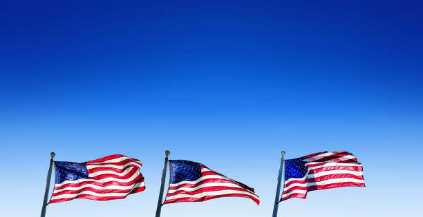 istock Waving three American flags in a row at flagpoles over sunny blue sky 2164067841