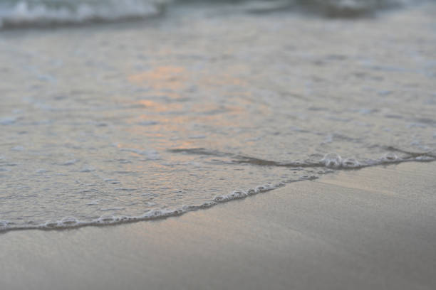 Sand beach background,Summer sea beach with wave  water splash on brown sandy texture for travel,vacation banner,Beautiful gloden hour sunlight reflection on  sea water and yellow beach sand