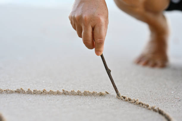 Close-up woman's hand drawing heart shape on sea sand.