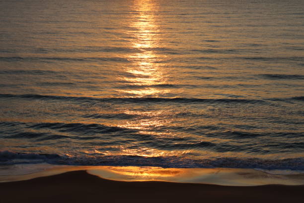 A morning sunrise casting an orange glow on the calm ocean in the early morning.