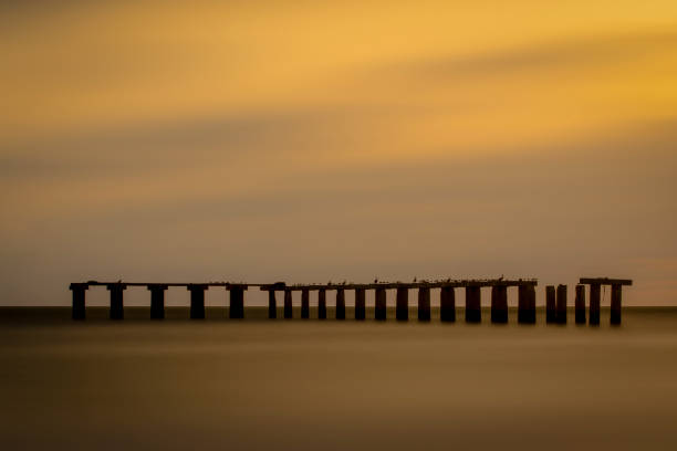 Boca Grande pier, now in ruins, very long exposure to smooth clouds and the Gulf of Mexico water in order to create a soft, tranquil look.  Pier is a silhouette against a late afternoon sky.