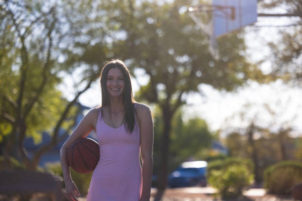 A young Gen Z girl with a basketball at the park on a basketball court.