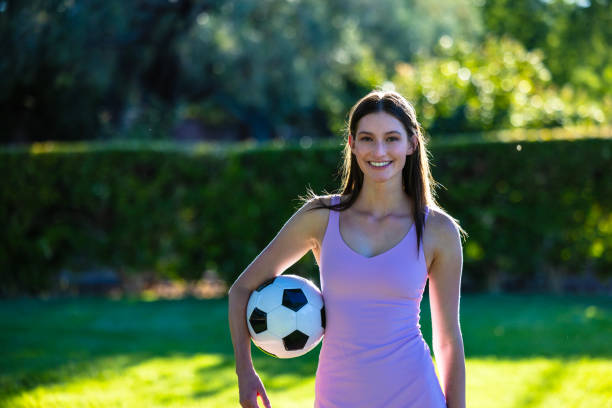 Full length / rear view / back of 20-29 years old adult beautiful brown hair / long hair caucasian female / young women soccer player / athlete / women's soccer kicking / juggling in front of white background wearing soccer uniform who is serious / confidence / concentration and holding ball / soccer ball / playing soccer - sport / sport / soccer field