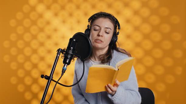 istock Narrator wearing headset reading aloud from book into mic, studio background 2164108476