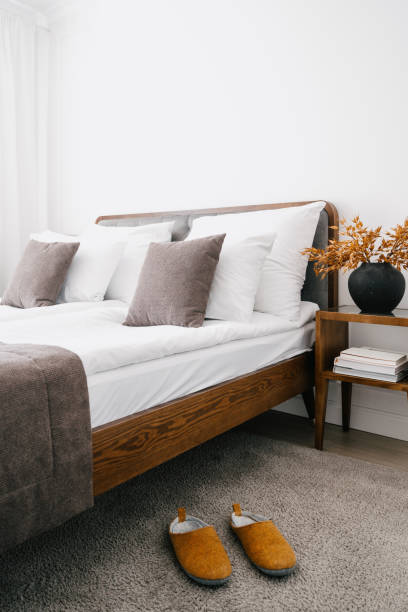 istock Orange home slippers on a soft carpet next to a comfortable bed and bedside table 2164110280
