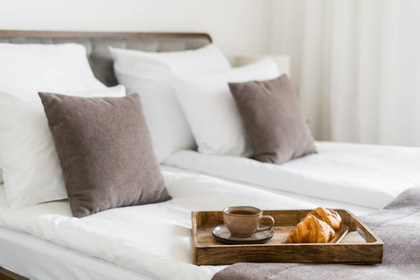 Mug with hot black coffee and fresh croissants for breakfast in bed Mug with hot black coffee and fresh croissants for breakfast in bed. French pastry and herbal tea on bedding linen in hotel bedroom with light interior. Meal served in room. Morning concepts bed breakfast pictures stock pictures, royalty-free photos & images