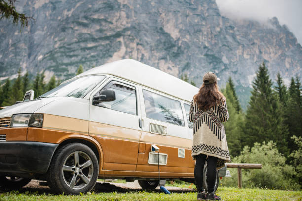 Happy young adventurer having her morning coffee on camping with van in nature.