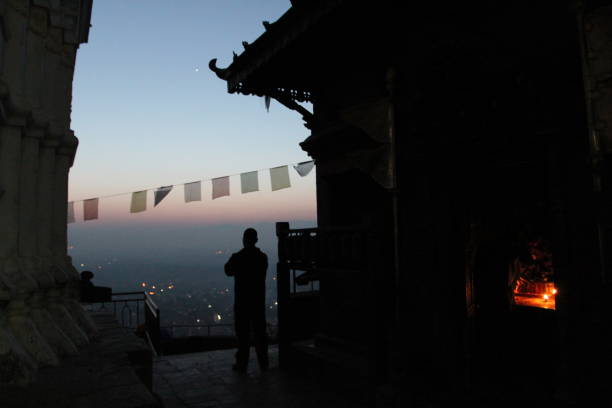 Kathmandu, Nepal. Taken December 1, 2012. Kathmandu Valley as seen from the top of the Swayambhunath temple in the morning fog as the sun comes up over the hills in the distance. Silhouette of people lining up to welcome the sunrise and temple is also visible.