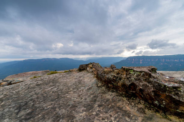 Elevated view of deep rugged valley and rolling hills from a rocky cliff edge. Gloomy day with dramatic cloudscape.