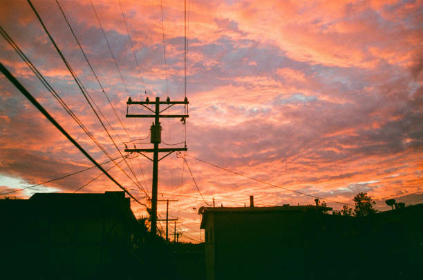 Power lines traverse a hilly landscape bordering a city on a cloudy afternoon.