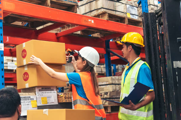 istock Warehouse management team use bar code scaner scan goods shelf writing checklist on clipboard. Asian men women worker check stock inventory. Teamwork logistics staff counting products store inventory 2164125669