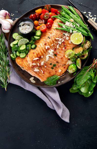 istock Cooked salmon with fresh vegetables, lime and souce. Baked fish on dark background 2164129333