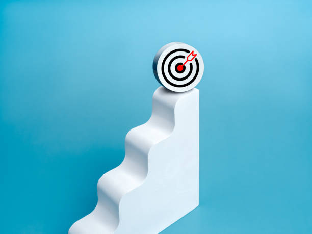 istock 3d target icon on top of white modern geometric bar graph chart steps, isolated on blue background, minimal style. Business growth, profit financial, investment, marketing goals and trends concepts. 2164130702
