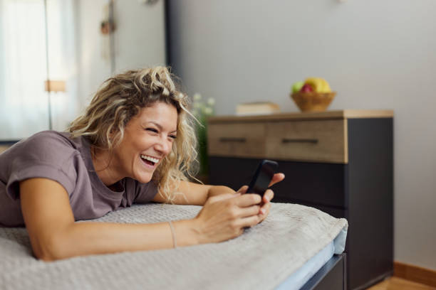 istock Happy woman using cell phone on a bed in bedroom. 2164135721