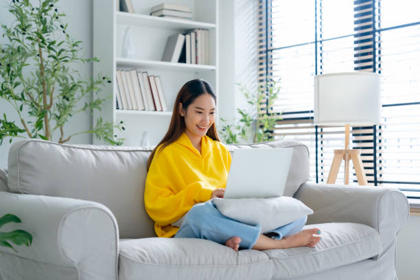 istock Happy young Asian woman using laptop while seated on couch at home 2164136317