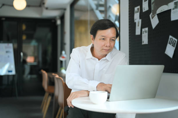 istock Smiling middle aged businessman using laptop at co working space 2164136932