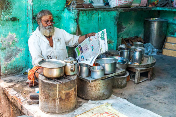 India, Uttar Pradesh, Varanasi. A man reading a newspaper while he cooks.