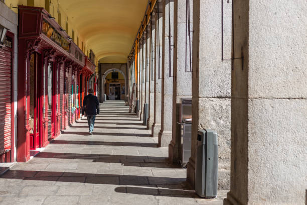 Madrid, Spain. A man walking under the arcades of Plaza Mayor in Madrid on a sunny morning.
