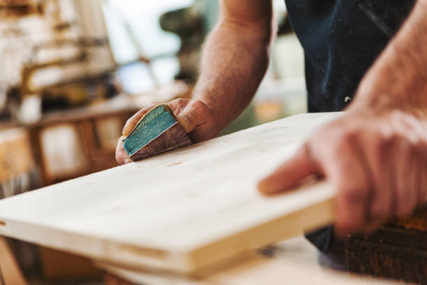 Carpenter sanding wood using sandpaper in workshop Carpenter is sanding a piece of wood in his workshop using sandpaper, his hands showing the strength and experience of a lifetime of craftsmanship sand paper stock pictures, royalty-free photos & images
