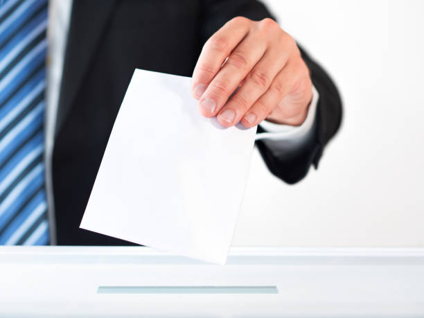 istock Man's hand putting ballot paper in voting box against white background 2164155595
