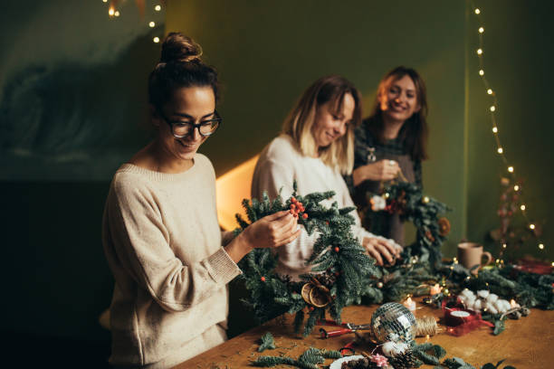 Happy women making Christmas wreath using natural pine branches and festive decorations.