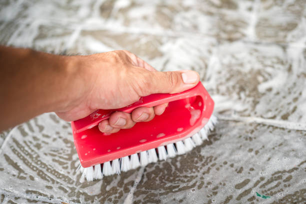 Action of janitor hand is using a scrub brush to scrubbing on granite rock floor. Home service job and hard working scene. Close-up with selective focus at the object.