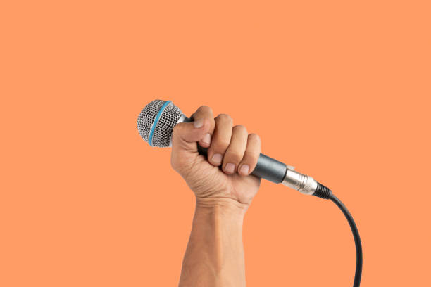 istock Black male hand holding a microphone isolated on orange background 2164162218