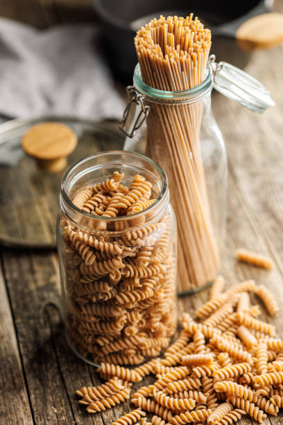 istock Uncooked whole grain pasta. Raw fusilli and spaghetti in jar on wooden table. 2164163473