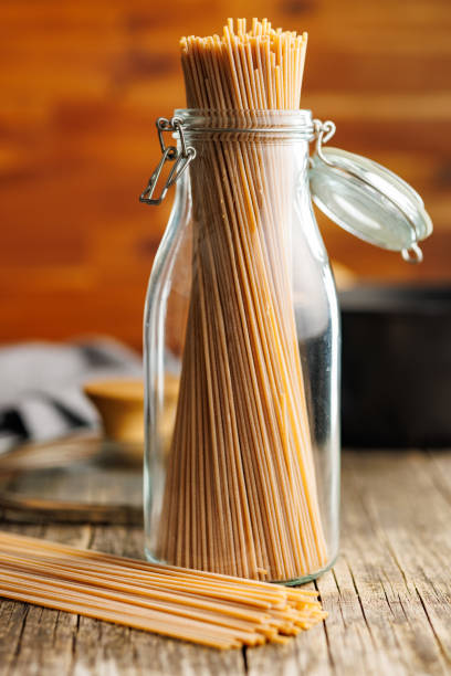 istock Uncooked whole grain pasta. Raw spaghetti in jar on wooden table. 2164163556
