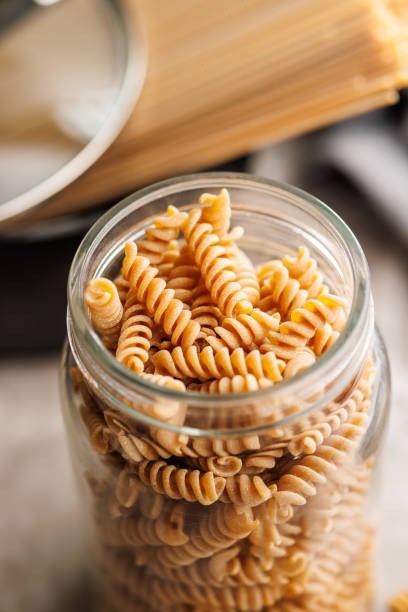 istock Uncooked whole grain pasta. Raw fusilli in jar on kitchen table. 2164163594