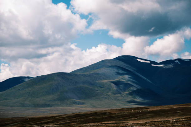 Remote mountain landscape in Rondane, Norway, with a gravel road leading through arctic tundra toward rugged peaks under dramatic clouds, symbol of wilderness and isolation.