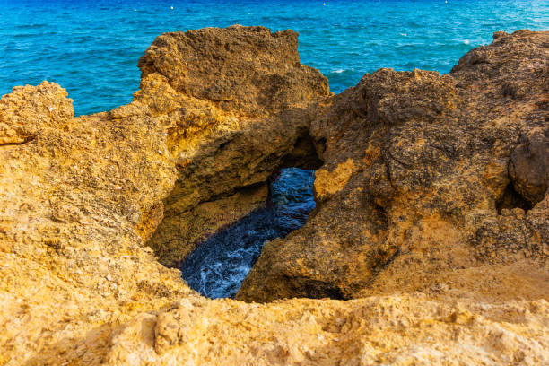 Ocean visible through a natural rock arch in Tarragona, surrounded by textured rock formations and vibrant blue waters.