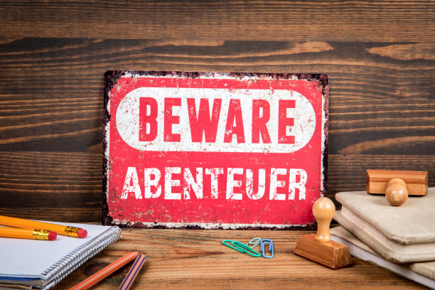 istock Adventure in German. Beware sign with text on a wooden texture office table 2164166376