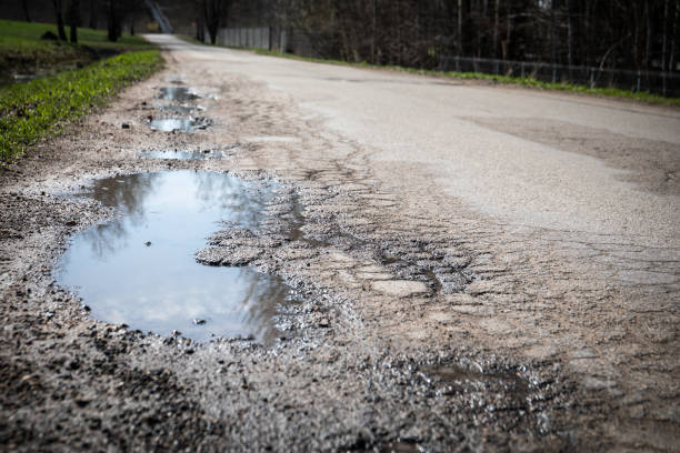 istock Puddles and damaged asphalt road edge. Sunny day 2164167925