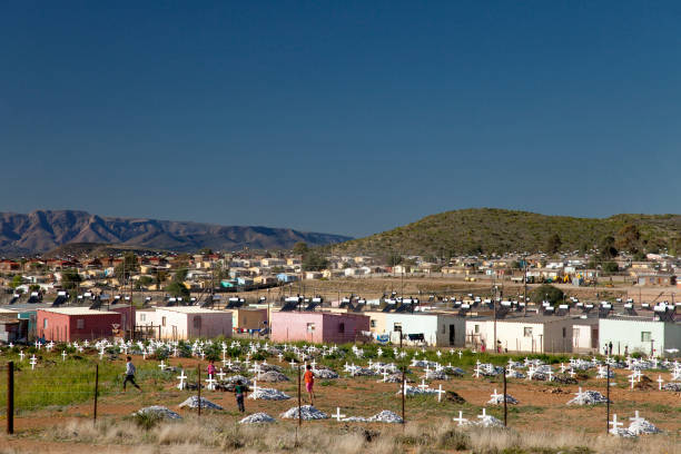 A rural village in the Western Cape near Cape Town sits among low hills, scattered houses, and green trees. Bright daylight reveals a peaceful countryside scene with natural vegetation, open space, and a calm, rural community atmosphere.
