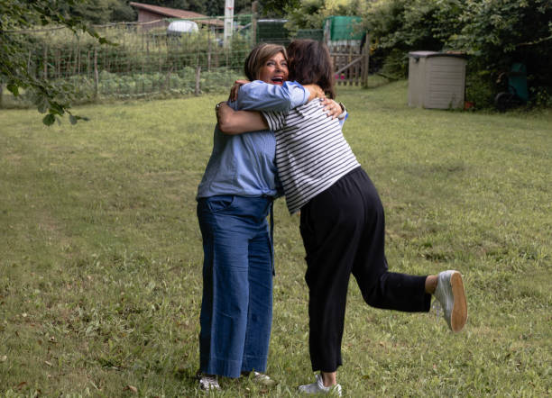 Two friends share a warm embrace upon arriving at a countryside picnic, celebrating their friendship in a lush green field.