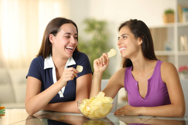 istock Happy roommates eating potato chips and talking at home 2164169476