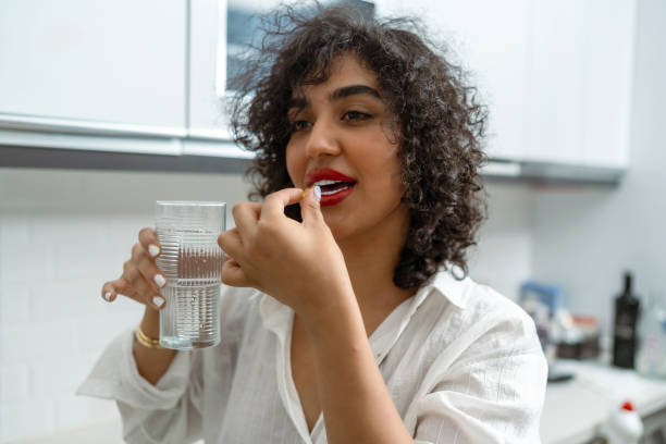 istock Curly haired woman drinks fish oil pills in the kitchen 2164170176