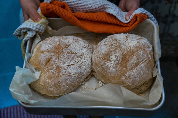 A woman beams with pride as she displays a freshly baked loaf of bread.