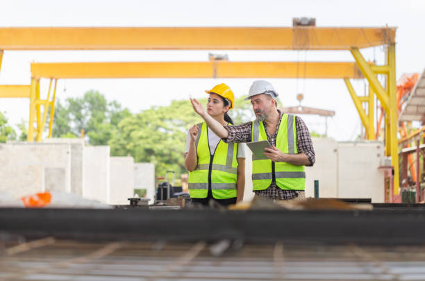 istock Caucasian engineer and female foreman worker with blueprints checking project at the precast concrete factory site, Engineer team in hardhats discussing on construction site 2164176414