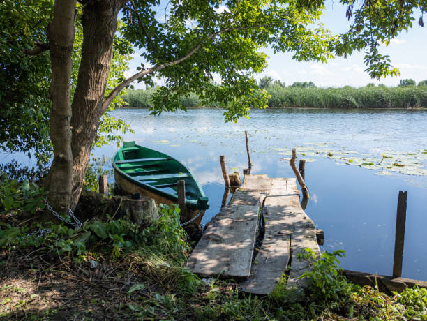istock Green boat near wooden dock, tranquil river scene 2164179364