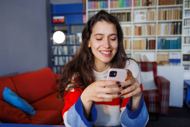 istock Young woman smiling while using smart phone at home 2164184365
