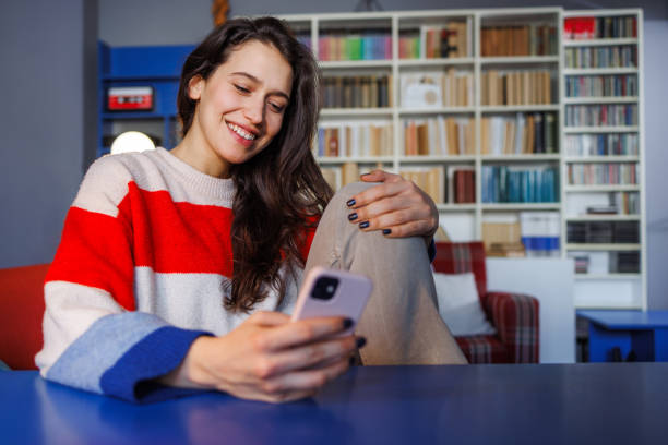 istock Young woman smiling while using smart phone in a cozy setting at home 2164184520