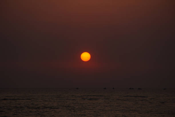 Stock photo showing an Indian man on holiday in Goa, South India, pictured walking on Palolem Beach, paddling in the gentle sea waves at sunset, a particularly popular winter holiday destination for both English and German tourists.