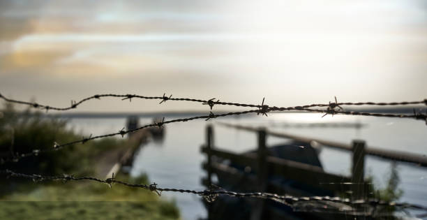 istock Simple barbed wire in front of a blurred waterscape with a murky sky 2164198718