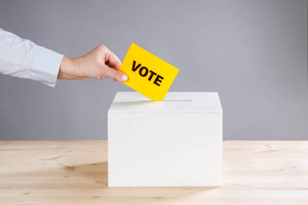 Woman's hand casting a vote and a ballot box. Vote on gray background