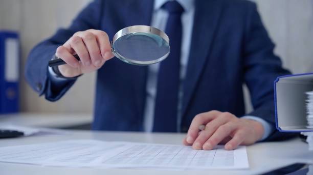 istock Businessman is carefully examining financial documents with a magnifying glass, highlighting the importance of thorough analysis in business. Audit and taxes 2164201857